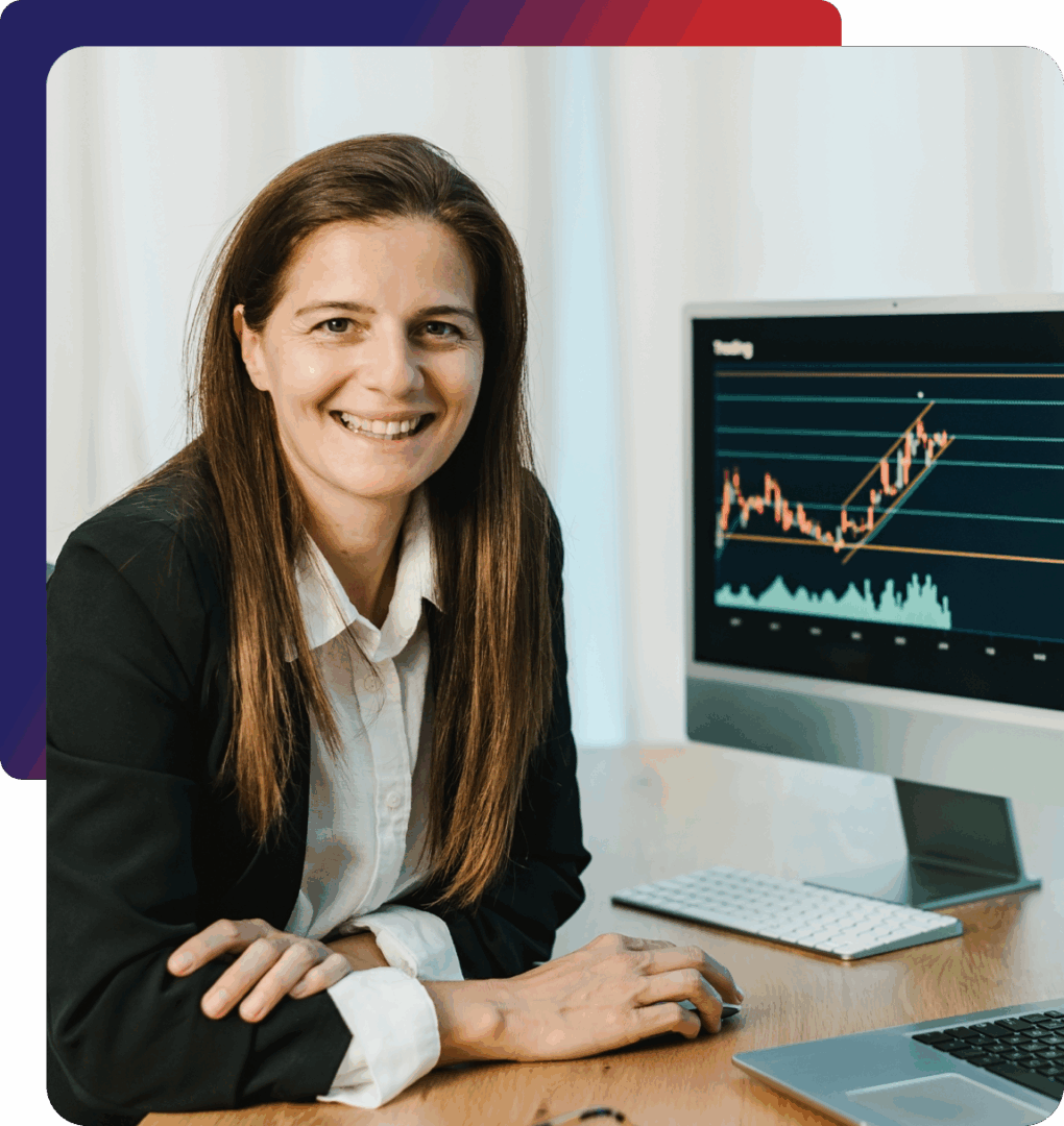 Smiling businesswoman sitting at desk with stock market chart on computer screen.
